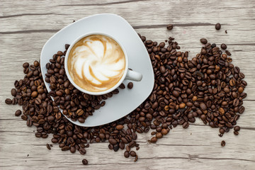 Cappuccino in weißer Tasse auf Holzuntergrund mit Kaffeebohnen
