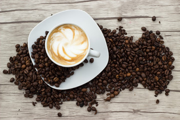 Cappuccino in weißer Tasse auf Holzuntergrund mit Kaffeebohnen