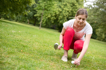 young woman placing a golf ball on a tee.