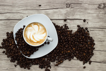 Cappuccino in weißer Tasse auf Holzuntergrund mit Kaffeebohnen