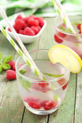 Raspberries and juice in glass on green wooden background
