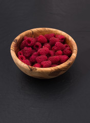 raspberries in a wooden bowl on black slate stone background 