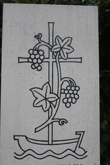 Grabstein mit schwarzem Kreuz, Boot und Weintrauben