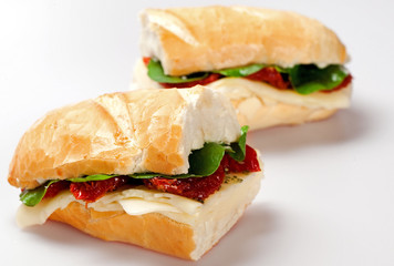 Sandwich on a white plate with turkey breast, tomato and lettuce.