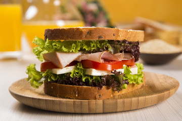 Sandwich on a white plate with turkey breast, tomato and lettuce.
