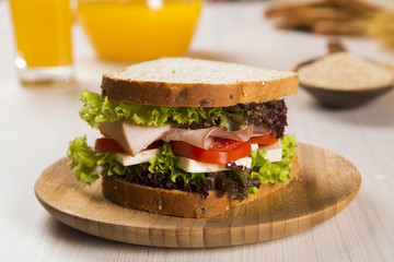 Sandwich on a white plate with turkey breast, tomato and lettuce.