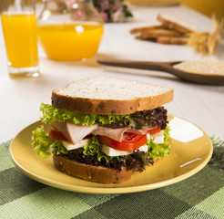 Sandwich on a white plate with turkey breast, tomato and lettuce.