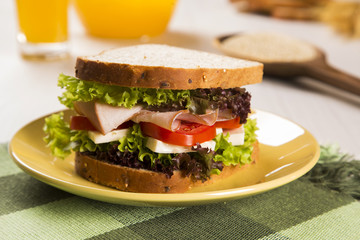 Sandwich on a white plate with turkey breast, tomato and lettuce.