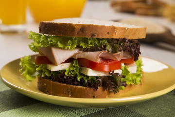 Sandwich on a white plate with turkey breast, tomato and lettuce.