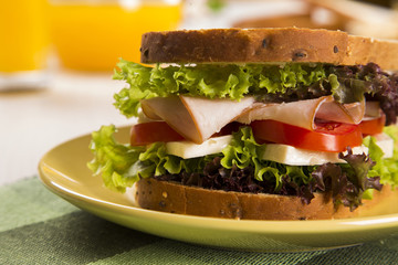 Sandwich on a white plate with turkey breast, tomato and lettuce.