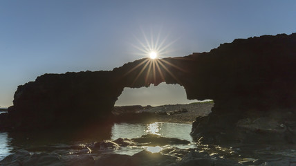 Obraz premium Sunrise atop the stone arch gate with bolt Sunstar Ly Son Island on rolling stone gate gives the feeling of the sun was playing.