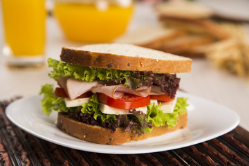 Sandwich on a white plate with turkey breast, tomato and lettuce.