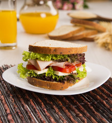 Sandwich on a white plate with turkey breast, tomato and lettuce.