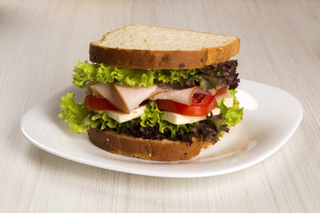 Sandwich on a white plate with turkey breast, tomato and lettuce.