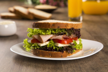 Sandwich on a white plate with turkey breast, tomato and lettuce.