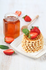 Jar of honey, ripe strawberries and waffles.