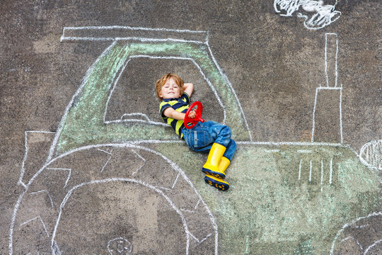 Little boy having fun with tractor picture drawing with chalk
