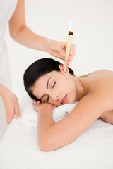 Fototapeta na wymiar Beautiful woman receiving ear candle treatment at spa center