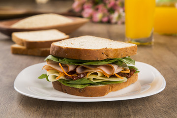Sandwich on a white plate with turkey breast, tomato and lettuce.