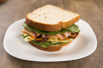 Sandwich on a white plate with turkey breast, tomato and lettuce