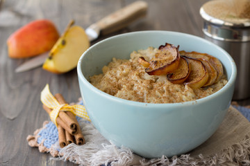 Oatmeal with baked apples and cinnamon in blue ceramic bowl on wooden table