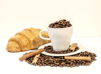 White cup with fresh coffee beans and french croissant