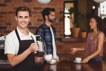 Smiling barista pouring milk into cup in front of customers