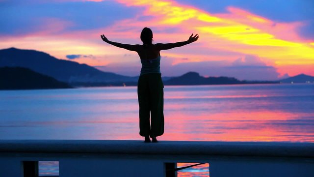 Beautiful sunset and young woman rising her hands into air. 