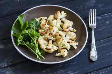 roasted cauliflower and fresh green salad on a brown plate on a dark wooden background