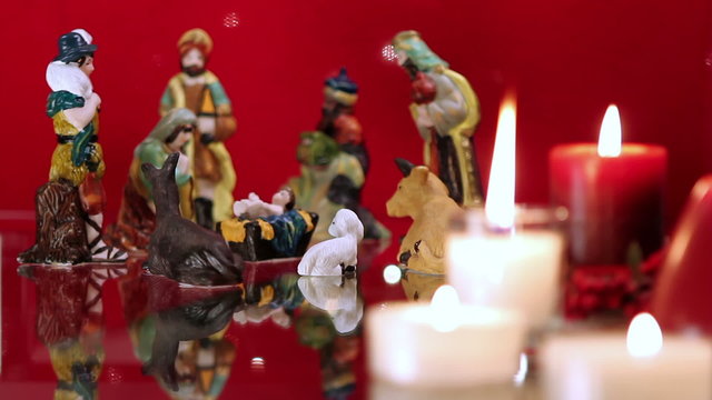 Christmas nativity scene with candles on red background with lights. The focus moves from candles to figurines.