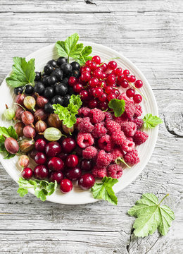 berries - raspberries, gooseberries, red currants, cherries, black currants on a white plate on a light wooden background