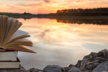 Stack of book and Open hardback book on blurred nature landscape backdrop against sunset sky with back light. Copy space, back to school. Education background.