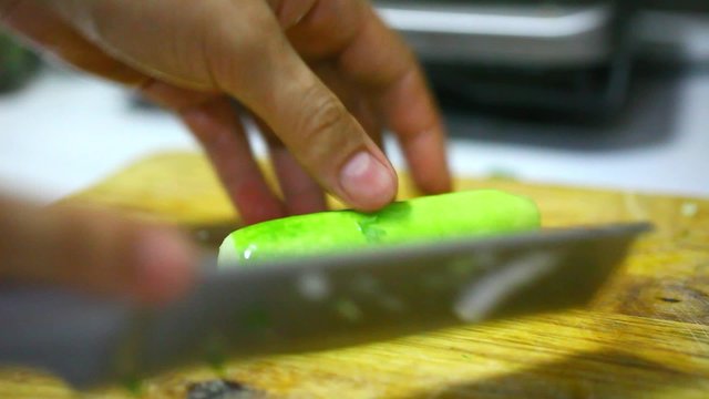 female hands chopping cucumber on a wooden board in the kitchen