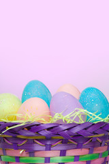 Easter Basket and Easter Eggs – An Easter basket filled with colored and speckled Easter eggs. Pink background.