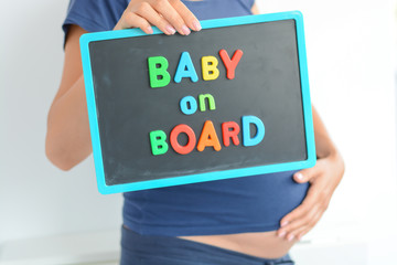 Pregnant woman holds a baby on board colored text on blackboard over her belly