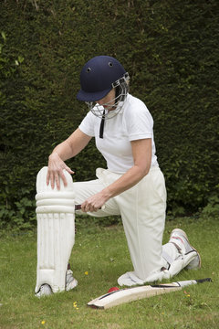 Elderly female cricketer fastens leg pads before going into bat