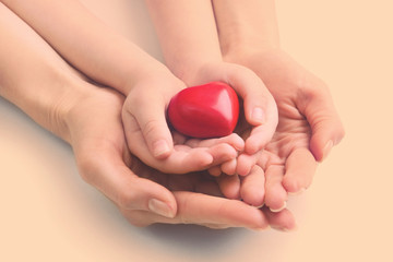 Heart in child and mother hands on light background