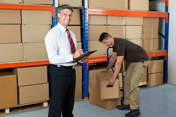 Manager With Clipboard And Worker In Warehouse