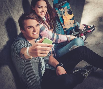 Young couple with skateboard  taking selfie outdoors