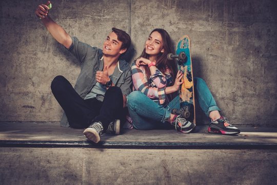 Young couple with skateboard  taking selfie outdoors