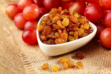 Raisins in bowl with grapes on table close up