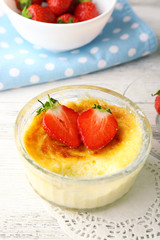 Creme brulee dessert with fresh strawberry berries on napkin, on color wooden background