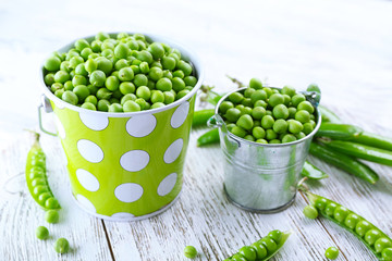 Fresh green peas in metal buckets on white wooden table, closeup