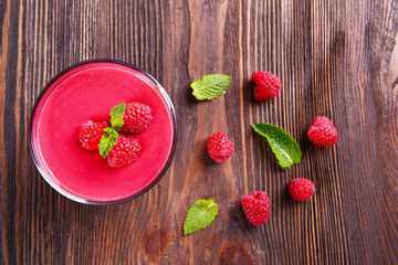 Glass of raspberry milk shake with berries on wooden table close up