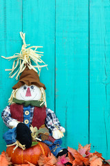 Scarecrow sitting on pumpkin by rustic wood fence