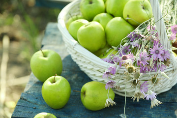 Green apples with bouquet of wildflowers on wooden table, closeup