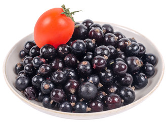Isolated black currant with tomato on saucer