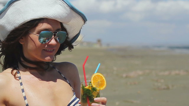 Closeup beautiful woman wearing sunglasses and hat, having long drink on beach