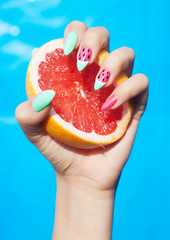 Hands close up of young woman with watermelon manicure holding slice of grapefruit summer manicure nails art and food concept  - 88139802