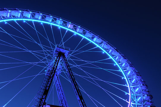 Ferris wheel with blue and light blue illumination against night sky - Powered by Adobe